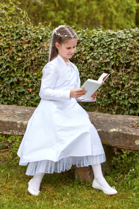 Kommunionkind Mädchen mit Buch auf einer Bank